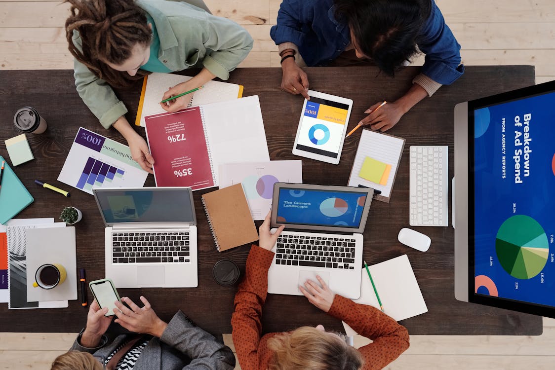 a group of people sitting around a table with laptops